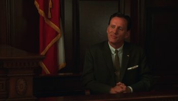 Movie still from “Ghosts of Mississippi” (1996), directed by Rob Reiner – A man in a suit sitting in front of a flag; Medium shot, Low angle