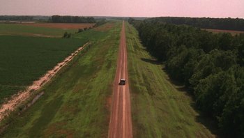 Movie still from “Ghosts of Mississippi” (1996), directed by Rob Reiner – An aerial view of a car driving down a dirt road; Extreme Wide shot, High angle