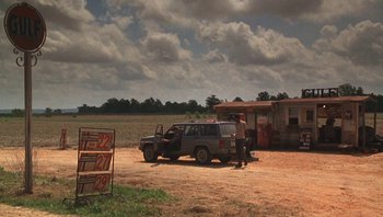 Movie still from “Ghosts of Mississippi” (1996), directed by Rob Reiner – A man standing next to an suv parked in a field; Extreme Wide shot, Over the shoulder angle