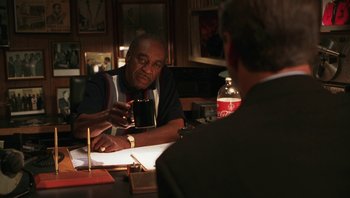 Movie still from “Ghosts of Mississippi” (1996), directed by Rob Reiner – A man sitting at a table in front of another man holding a drink; Medium shot, Over the shoulder angle