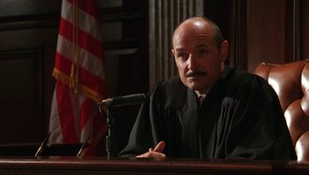 Movie still from “Ghosts of Mississippi” (1996), directed by Rob Reiner – A man in a robe is sitting at a podium; Close Up shot, High angle