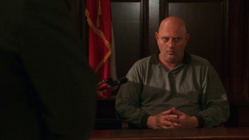 Movie still from “Ghosts of Mississippi” (1996), directed by Rob Reiner – A man sitting in front of a microphone in a courtroom; Medium shot, Low angle
