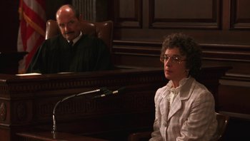 Movie still from “Ghosts of Mississippi” (1996), directed by Rob Reiner – An older woman sitting in front of a judge in a courtroom; Medium shot, Over the shoulder angle