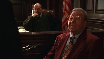 Movie still from “Ghosts of Mississippi” (1996), directed by Rob Reiner – An older man in a red suit sitting in front of a judge; Medium shot, Low angle