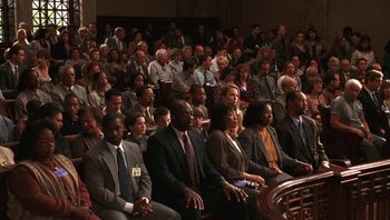Movie still from “Ghosts of Mississippi” (1996), directed by Rob Reiner – A group of people sitting in front of an audience at an event; Wide shot, High angle