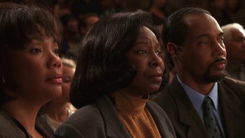 Movie still from “Ghosts of Mississippi” (1996), directed by Rob Reiner – A group of people sitting in front of a crowd of people; Close Up shot, Low angle
