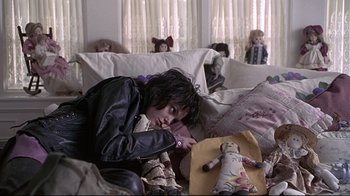 Movie still from “Gia” (1998), directed by Michael Cristofer – A person sitting on a couch with a doll; Wide shot, High angle