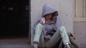 Movie still from “Gia” (1998), directed by Michael Cristofer – A person sitting on the ground holding a cup; Medium shot, High angle