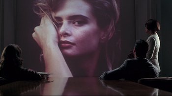 Movie still from “Gia” (1998), directed by Michael Cristofer – A person sitting on a table next to an image of a woman's face; Wide shot, Over the shoulder angle