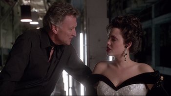 Movie still from “Gia” (1998), directed by Michael Cristofer – A man and a woman in a room with lights in the background; Medium shot, Over the shoulder angle