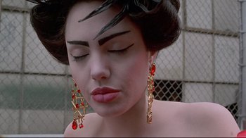 Movie still from “Gia” (1998), directed by Michael Cristofer – A woman with long red earrings and black eyeliner on her face; Close Up shot, Low angle