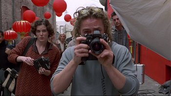 Movie still from “Gia” (1998), directed by Michael Cristofer – A man taking a picture with a camera in front of a crowd; Medium shot, Low angle