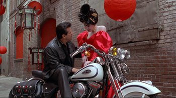 Movie still from “Gia” (1998), directed by Michael Cristofer – A man sitting on the back of a motorcycle next to a woman; Medium shot, Over the shoulder angle