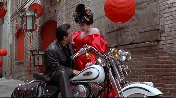 Movie still from “Gia” (1998), directed by Michael Cristofer – A man sitting on a motorcycle next to a beautiful woman; Medium shot, Low angle