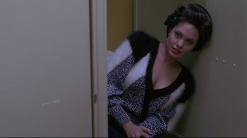 Movie still from “Gia” (1998), directed by Michael Cristofer – A woman sitting in front of a door looking at the camera; Medium shot, Over the shoulder angle