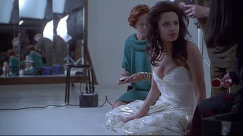 Movie still from “Gia” (1998), directed by Michael Cristofer – A woman sitting on the ground while another woman is sitting on the floor holding a remote; Medium shot, Over the shoulder angle