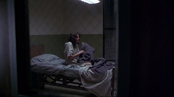 Movie still from “Gia” (1998), directed by Michael Cristofer – A woman sitting on a bed holding a pair of socks; Wide shot, High angle