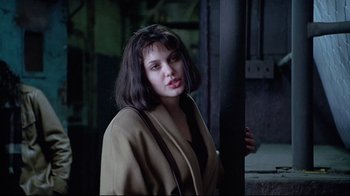 Movie still from “Gia” (1998), directed by Michael Cristofer – A woman in a tan jacket standing next to a pole; Close Up shot, Over the shoulder angle