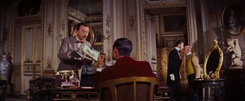 Movie still from “Gigi” (1958), directed by Vincente Minnelli – A man in a suit and bow tie sitting in front of a man in a suit and bow tie in front of a mirror; Medium shot, Low angle