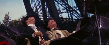 Movie still from “Gigi” (1958), directed by Vincente Minnelli – A man in a suit and a hat sitting in front of a microphone; Medium shot, Low angle