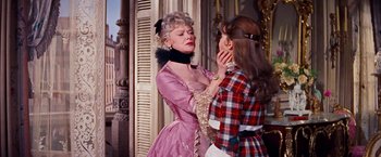 Movie still from “Gigi” (1958), directed by Vincente Minnelli – Two women dressed in period clothing , one of which is holding her hand to the other's face; Medium shot, Over the shoulder angle