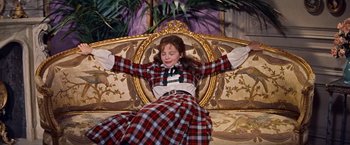 Movie still from “Gigi” (1958), directed by Vincente Minnelli – A woman sitting on top of a couch with her arms outstretched; Medium shot, High angle