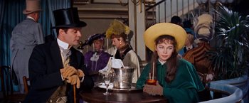 Movie still from “Gigi” (1958), directed by Vincente Minnelli – A group of people sitting at a table with drinks; Medium shot, Over the shoulder angle
