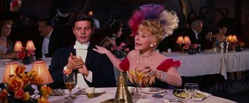 Movie still from “Gigi” (1958), directed by Vincente Minnelli – An older woman wearing a hat and a dress at a dinner table; Medium shot, Over the shoulder angle