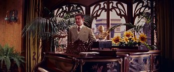 Movie still from “Gigi” (1958), directed by Vincente Minnelli – A man standing in front of a desk in a room; Medium shot, Over the shoulder angle