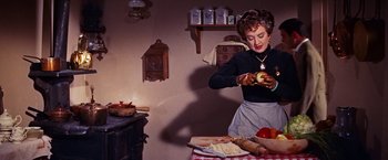 Movie still from “Gigi” (1958), directed by Vincente Minnelli – A woman in a black shirt is cutting an apple in a kitchen; Medium shot, Low angle