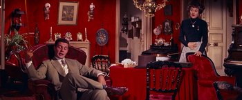 Movie still from “Gigi” (1958), directed by Vincente Minnelli – A man sitting on a chair in a living room next to a fire place; Wide shot, High angle