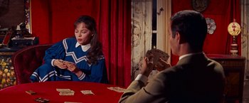 Movie still from “Gigi” (1958), directed by Vincente Minnelli – A woman in a cheerleader uniform is playing cards with a man in a suit in front of a red curtain; Medium shot, Over the shoulder angle