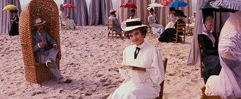 Movie still from “Gigi” (1958), directed by Vincente Minnelli – A woman sitting on a chair on the beach holding a plate; Wide shot, High angle