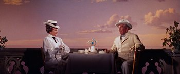 Movie still from “Gigi” (1958), directed by Vincente Minnelli – A couple of people sitting at a table with a cup; Medium shot, Low angle