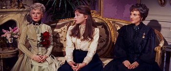 Movie still from “Gigi” (1958), directed by Vincente Minnelli – A woman sitting on top of a couch wearing a white shirt; Medium shot, High angle