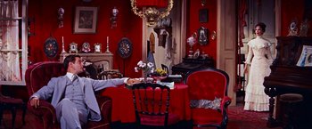 Movie still from “Gigi” (1958), directed by Vincente Minnelli – A living room filled with furniture and a red wall; Wide shot, High angle