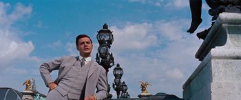 Movie still from “Gigi” (1958), directed by Vincente Minnelli – A man in a suit and tie standing next to street lights; Medium shot, Low angle