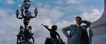 Movie still from “Gigi” (1958), directed by Vincente Minnelli – A man standing next to a statue of a man with a gun; Wide shot, Low angle