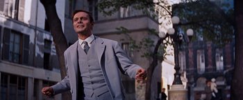 Movie still from “Gigi” (1958), directed by Vincente Minnelli – A man in a suit and tie standing on a sidewalk; Medium shot, Low angle