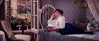 Movie still from “Gigi” (1958), directed by Vincente Minnelli – A woman sitting on top of a bed next to a cat; Medium shot, High angle