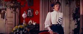 Movie still from “Gigi” (1958), directed by Vincente Minnelli – A woman standing in a room with a red wall; Medium shot, Over the shoulder angle