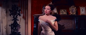 Movie still from “Gigi” (1958), directed by Vincente Minnelli – A woman in a white dress standing in front of a fireplace; Medium shot, Low angle