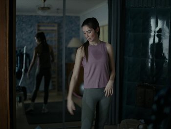 Movie still from “Girl Picture” (2022), directed by Alli Haapasalo – A woman is standing in front of a mirror in a room; Medium shot, Over the shoulder angle