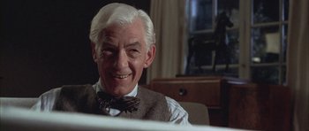 Movie still from “Gods and Monsters” (1998), directed by Bill Condon – An older man sitting at a table with a smile on his face; Close Up shot, Low angle