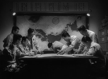 Movie still from “Godzilla” (1954), directed by Ishirô Honda – A black and white photo of a group of people looking at a map; Medium shot, High angle