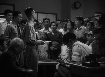 Movie still from “Godzilla” (1954), directed by Ishirô Honda – A group of people standing around a table; Medium shot, High angle