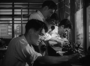 Movie still from “Godzilla” (1954), directed by Ishirô Honda – A black and white photo of a group of men working on phones; Medium shot, Low angle