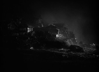 Movie still from “Godzilla” (1954), directed by Ishirô Honda – A black - and - white photo of houses on a cliff; Extreme Wide shot, High angle