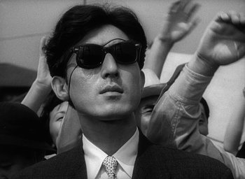 Movie still from “Godzilla” (1954), directed by Ishirô Honda – A black and white photo of a man wearing sunglasses; Close Up shot, Low angle