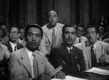 Movie still from “Godzilla” (1954), directed by Ishirô Honda – A black and white photo of a group of men in suits; Medium shot, Low angle
